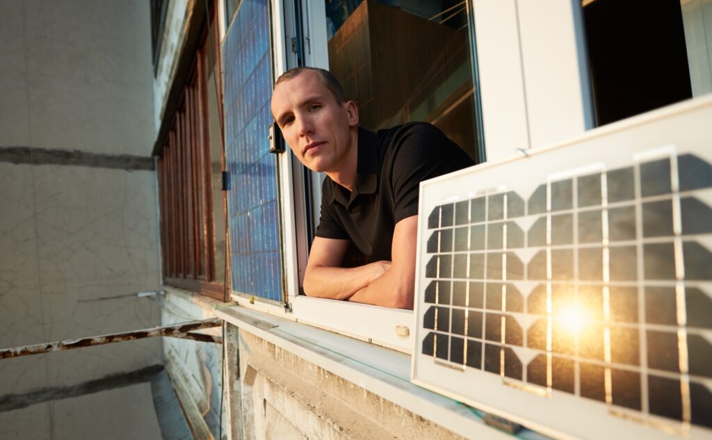 man on balcony of residential building with solar panel in which the sun is reflected at sunset